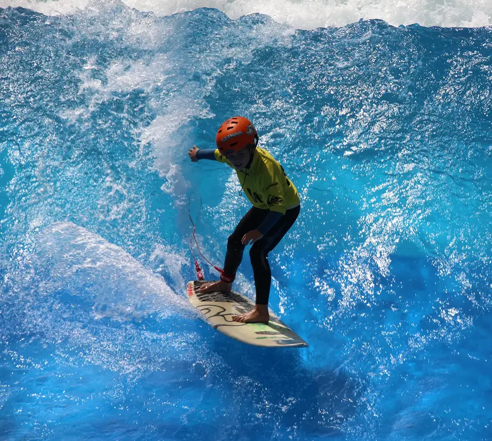 Junger Surfer steht mit seinem orangenen Helm auf der irie surf Welle